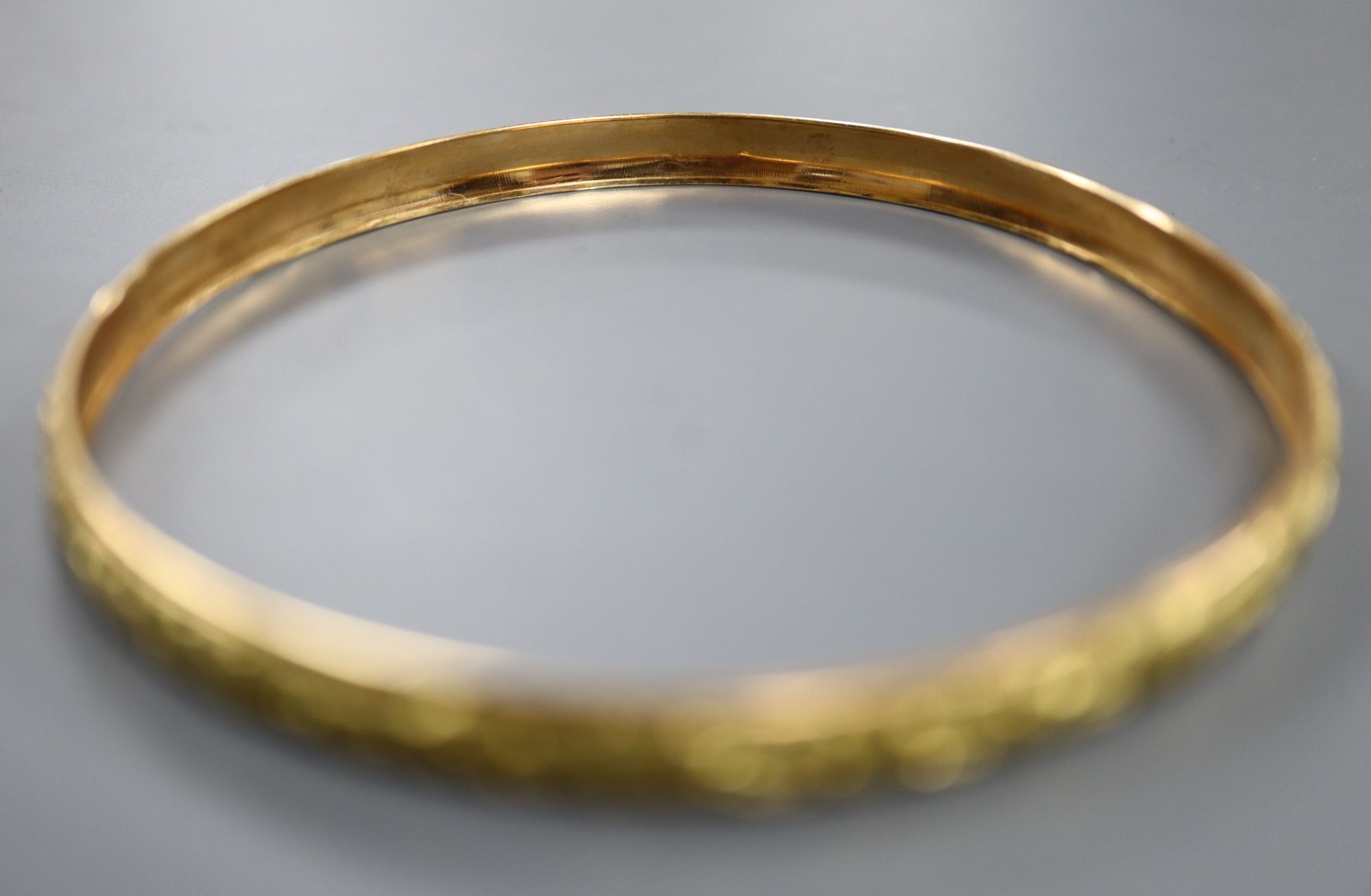 A yellow metal (tests as 18ct) bangle cast with continuous band of flowers, 9g,